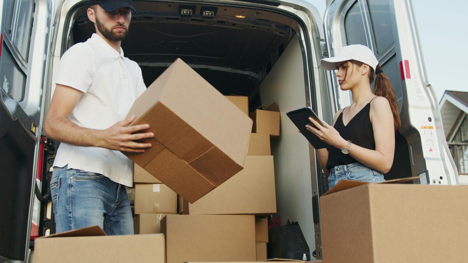 Man and woman working together, checking boxes behind a van.