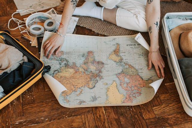 A woman with tattoos spreads out a vintage map on a wooden floor.