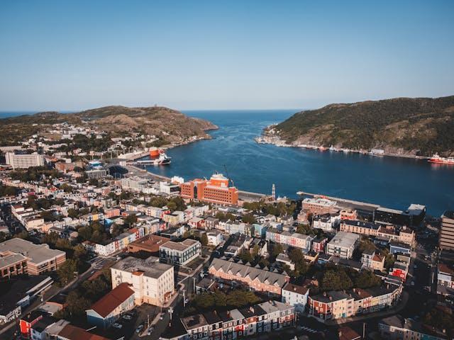 A peaceful Newfoundland town with colorful homes, rolling green hills, and a serene bay, embodying the calm and relaxed atmosphere of the island