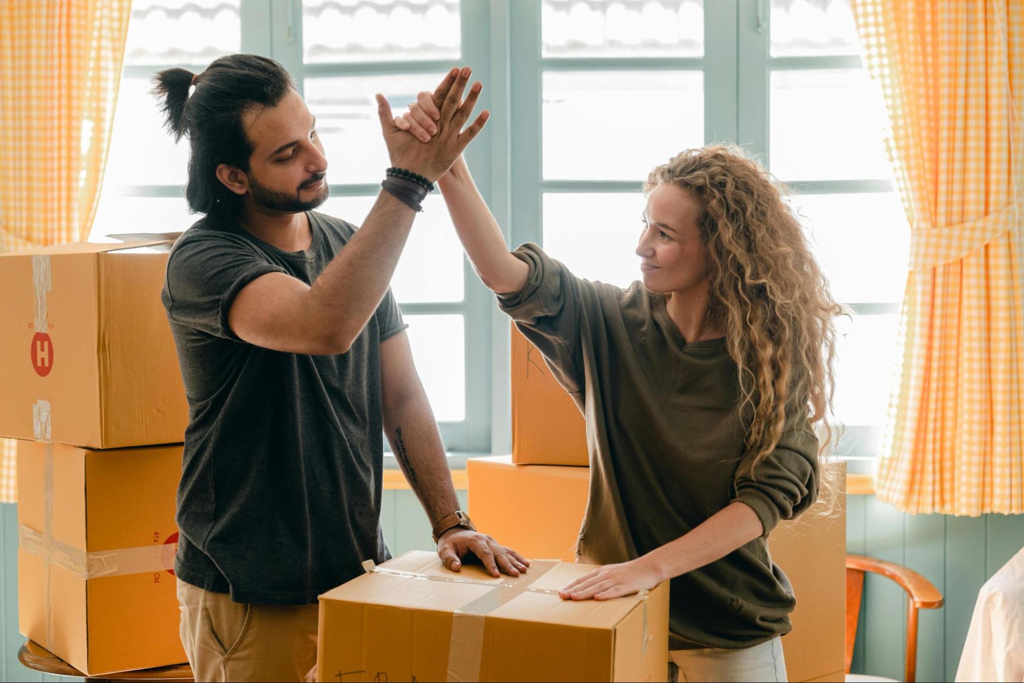 A  couple giving each other a high-five in a room filled with moving boxes, symbolizing the excitement of their upcoming move to a new home.